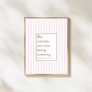 May include: A framed print with a light wood frame. The print features a pink and white striped background. In the center is a green-bordered rectangle with the text "His mercies are new every morning" and the reference "Lamentations 3:22-23".