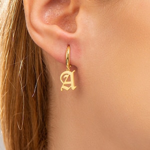 May include: Gold hoop earrings with a dangling letter 'A' charm in an old English font.