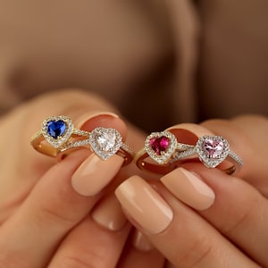 May include: Three gold rings with heart-shaped settings. The rings feature a blue, white, and pink gemstone in each setting. The rings are set with smaller clear gemstones around the larger centre gemstone.