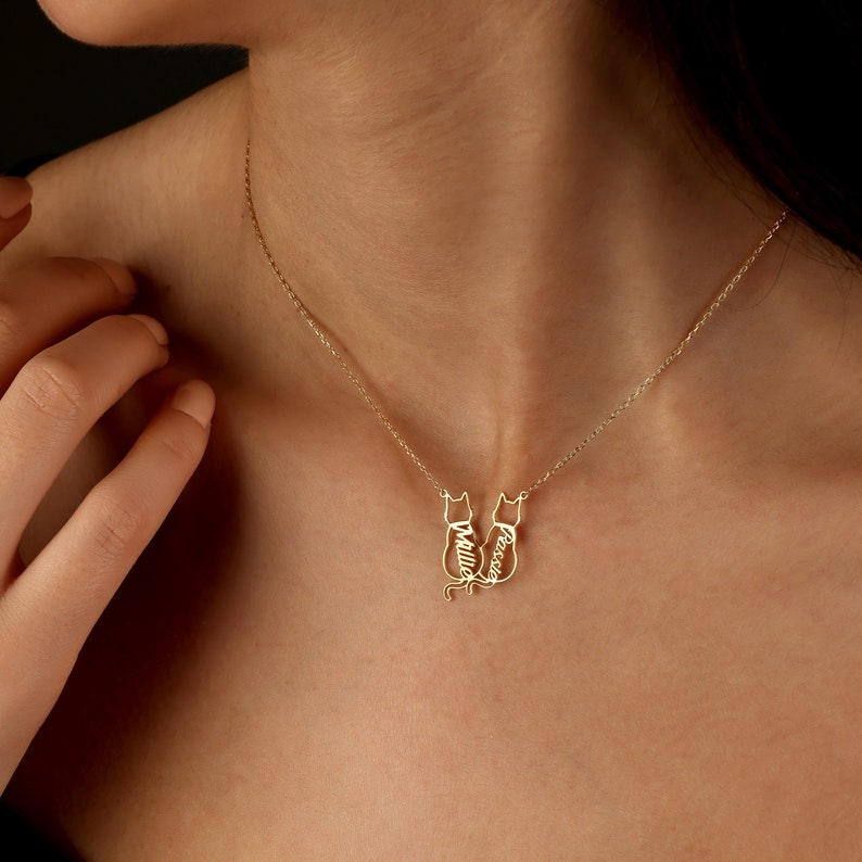 Pu&ograve; includere: Collana d'oro con un ciondolo che rappresenta due gatti che si guardano. I gatti sono delineati e i nomi " Millie" e " Rosie" sono scritti all'interno dei contorni.