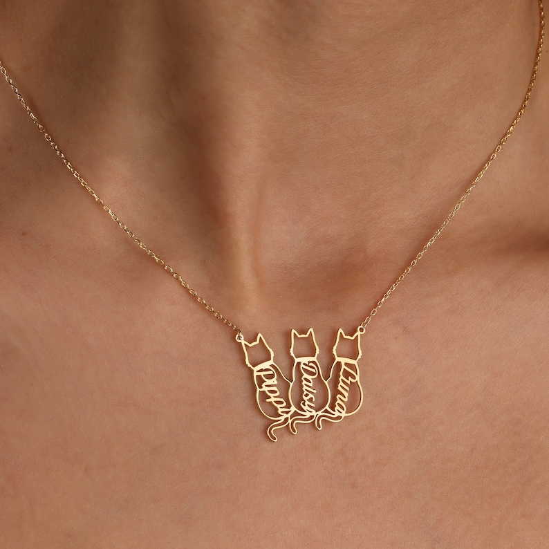 Pu&ograve; includere: Collana in oro con tre silhouette di gatti, ciascuna con un nome inciso: Luna, Daisy e Pippy.