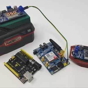 Pode incluir: Uma variedade de componentes eletrônicos, incluindo placas de circuito, um regulador de tensão com um display digital mostrando "5.0" e um pacote de bateria preto e vermelho. Um fio verde e amarelo conecta a bateria ao regulador de tensão.