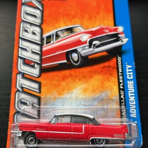 May include: A red and white Matchbox Cadillac Fleetwood toy car on a blue and orange card. The card reads "Matchbox" and "Adventure City". The toy car is a miniature replica of a classic car.