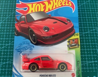 May include: Red Hot Wheels die-cast toy car model of a Porsche 993 GT2. The car is on a white background with a blue and yellow Hot Wheels logo. The car is part of the HW Exotics series and is numbered 174/250.