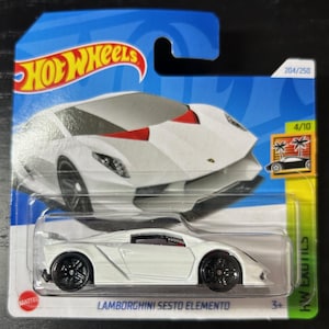 May include: A white Hot Wheels die-cast toy car of a Lamborghini Sesto Elemento. The car is on a blue and white background with the Hot Wheels logo. The car is numbered 204/250 and 4/10. The car is labeled "Lamborghini Sesto Elemento".