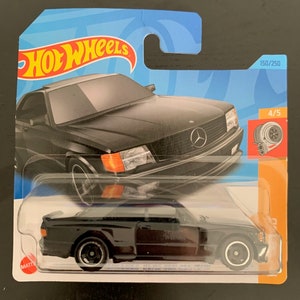 May include: Black Hot Wheels die-cast toy car model of a Mercedes-Benz 560 SEC AMG. The car is on a blue and orange card with the Hot Wheels logo and the number 150/250. The car has a black body and black wheels.