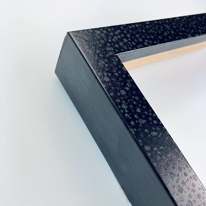 May include: Close-up of a black picture frame with a textured surface. The frame has a subtle speckled pattern.