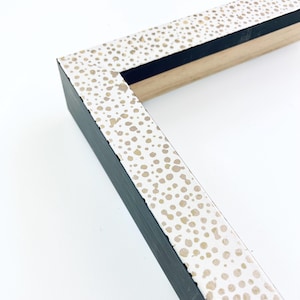 May include: Close-up of a white picture frame with a black border. The frame has a gold speckled pattern on the white surface.