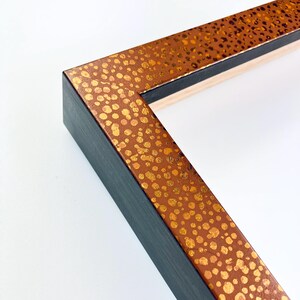 May include: Close-up of a picture frame with a brown wood frame and a gold speckled design.