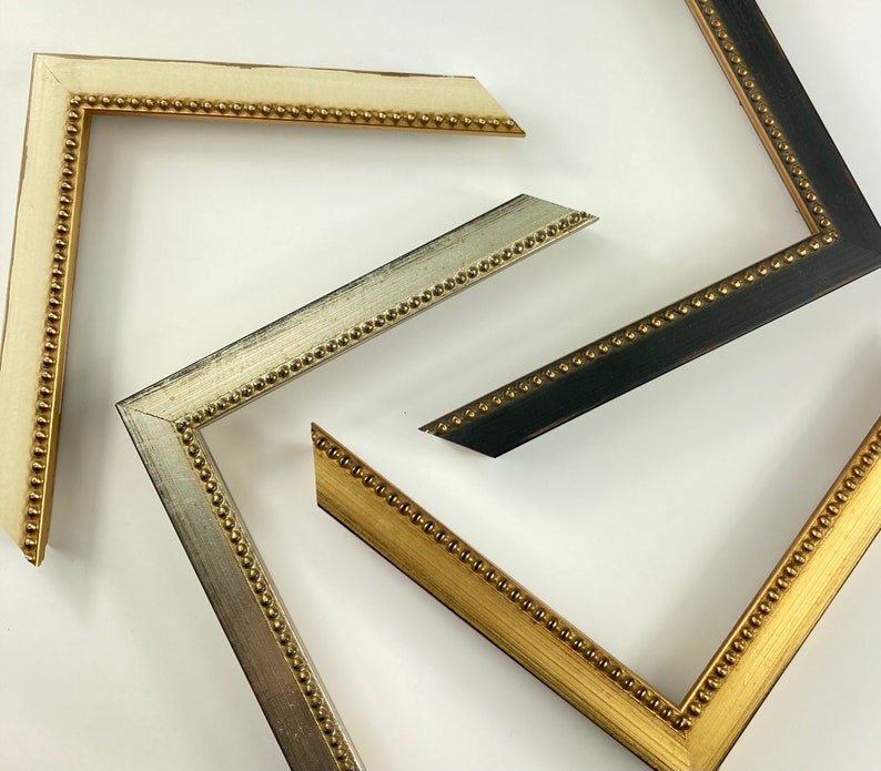 May include: Three picture frames with ornate gold trim and beaded edges. The frames are in different sizes and colours: white, silver, and black.