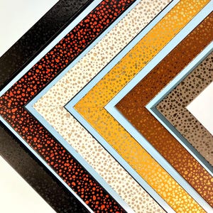 May include: Five picture frames with different colored speckled patterns. The frames are arranged in a pyramid shape with the largest frame at the bottom and the smallest frame at the top. The frames are black, red, white, gold, and brown.