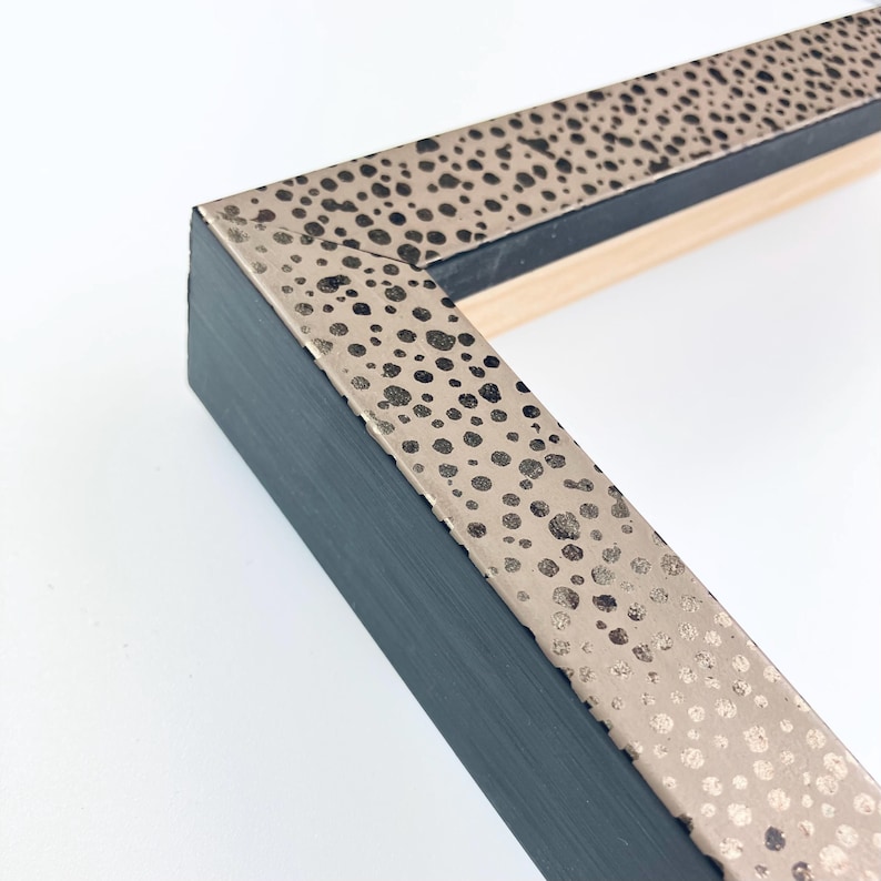 May include: Close-up of a black picture frame with a gold speckled border. The frame is made of wood and has a simple, modern design.