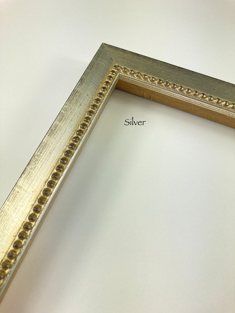 May include: Close-up of a silver picture frame with a gold beaded trim. The frame is on a white background. "Silver" is written in black text on the frame.