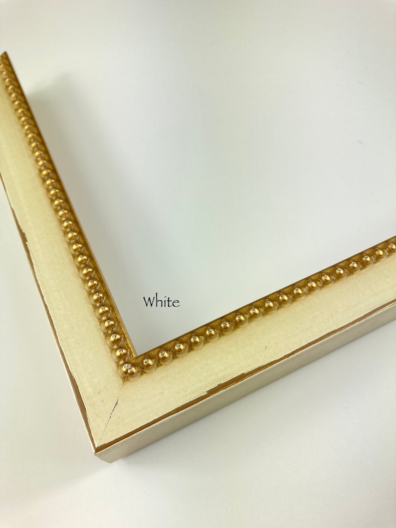 May include: Close-up of a white picture frame with a gold beaded trim. The frame is labelled "White".