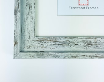 May include: Close-up of the corner of a white wood picture frame with a distressed finish. The frame has a simple, clean design. The text "Fernwood Frames" is visible in the upper right corner of the image.