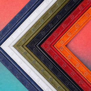 May include: A collection of colorful picture frames in various shades, including navy blue, white, olive green, black, red, and orange. Each frame has a decorative floral pattern along the edges, creating a visually appealing display.