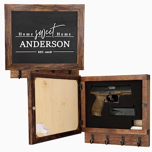 May include: A wooden wall-mounted gun safe with a chalkboard top. The chalkboard reads "Home Sweet Home ANDERSON EST. 2018". The safe has a compartment with a handgun and magazine, and a key hook rack.