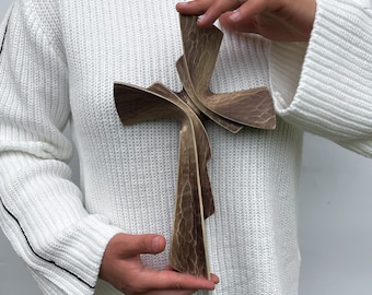 Peut inclure: Une croix en bois brun présentant une surface sculptée et texturée avec des courbes fluides et superposées. La croix possède une finition sombre et patinée avec des motifs de grain de bois visibles et une forme sculpturale distincte.