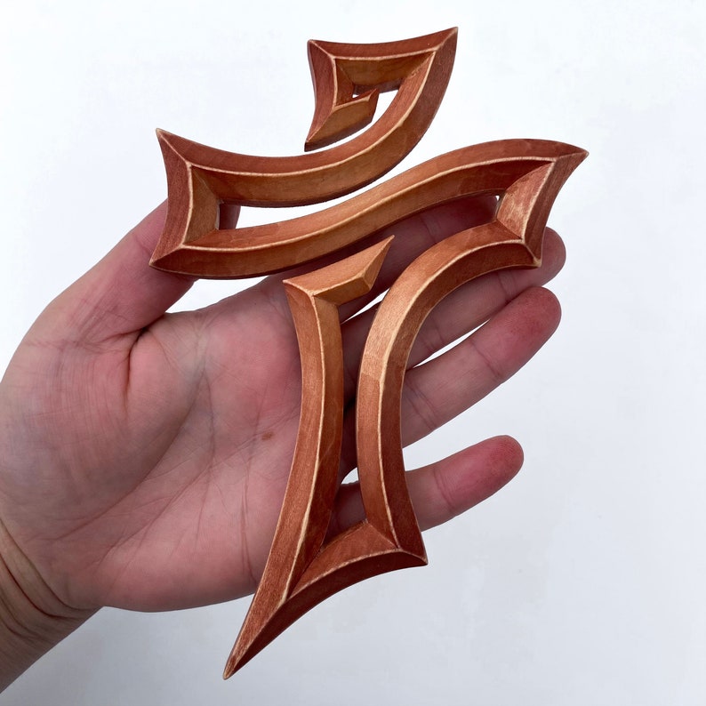 Peut inclure: Une croix en bois avec un design unique et complexe. La croix est en bois brun clair et a une finition lisse et polie.