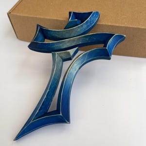 Peut inclure: Une croix en bois bleue avec un design abstrait unique. La croix est faite de plusieurs couches de bois, cr&eacute;ant un effet tridimensionnel.