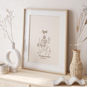 Puede incluir: Impresión enmarcada con un fondo beige, que representa un dibujo lineal de una deidad montada en un animal, con la palabra "Agni" arriba y texto abajo. El marco de madera clara está sobre una superficie de madera, junto a jarrones decorativos.
