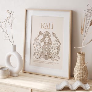 Könnte beinhalten: Ein gerahmter Druck mit beigefarbenem Hintergrund, der eine Linienzeichnung von Kali, einer hinduistischen Göttin, mit mehreren Armen zeigt, die Waffen halten. Der Text "KALI" befindet sich oben auf dem Druck. Der Text unter dem Bild lautet "Kali, die Göttin der Zeit und der Ermächtigung, hilft dir, deine Ängste zu besiegen und deine innere Stärke freizusetzen."