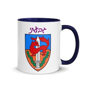 May include: White ceramic mug with a blue rim and handle. The mug features a colorful illustration of a red fox with a sword, surrounded by green cactus plants. The text "Jerez" is written in purple above the illustration.