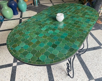 Puede incluir: Una mesa ovalada verde con una tapa de mosaico y una base de hierro forjado negro. La mesa está sobre un suelo de ajedrez.