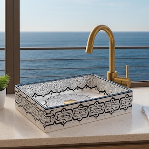 May include: A rectangular ceramic sink with a black and white patterned design, a gold faucet, and a small potted plant. The sink is on a countertop with a view of the ocean.