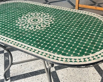 Puede incluir: Mesa ovalada con tapa de mosaico de azulejos verdes y blancos. La mesa tiene un marco y patas de metal negro.