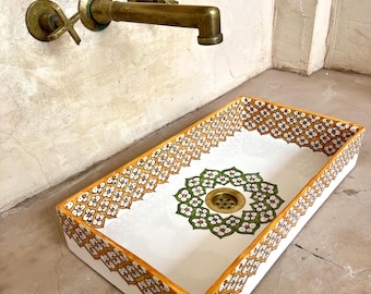 Puede incluir: Un lavabo de cerámica blanca con un patrón floral decorativo naranja y verde alrededor del borde. El lavabo tiene un desagüe de latón y está montado en una pared.