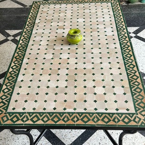 May include: A square, white tiled table with a green and brown border. The table has a black metal frame and is sitting on a black and white checkered floor.
