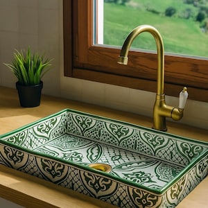 May include: Rectangular ceramic sink with a green and white patterned design. The sink is installed on a wooden countertop, with a gold tap and a small potted plant in the background. The sink's dimensions are not visible.