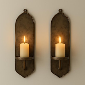 May include: Two wall-mounted candle holders with lit candles. The holders are bronze-colored with an arched top and a circular base to hold the candle. The candles are white and cylindrical, with a bright flame.