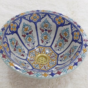May include: A white ceramic sink with a blue, yellow, and red floral pattern. The sink has a brass drain.