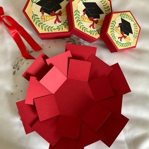 May include: Three red and white graduation themed gift boxes with a black graduation cap and diploma design. The boxes are open and folded flat, revealing a red paper hexagon.