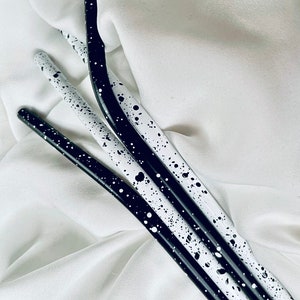 May include: Four slender, curved metal straws with a speckled black and white design. The straws are arranged diagonally against a white background, creating a visually appealing contrast. The design features a pattern of black and white spots.