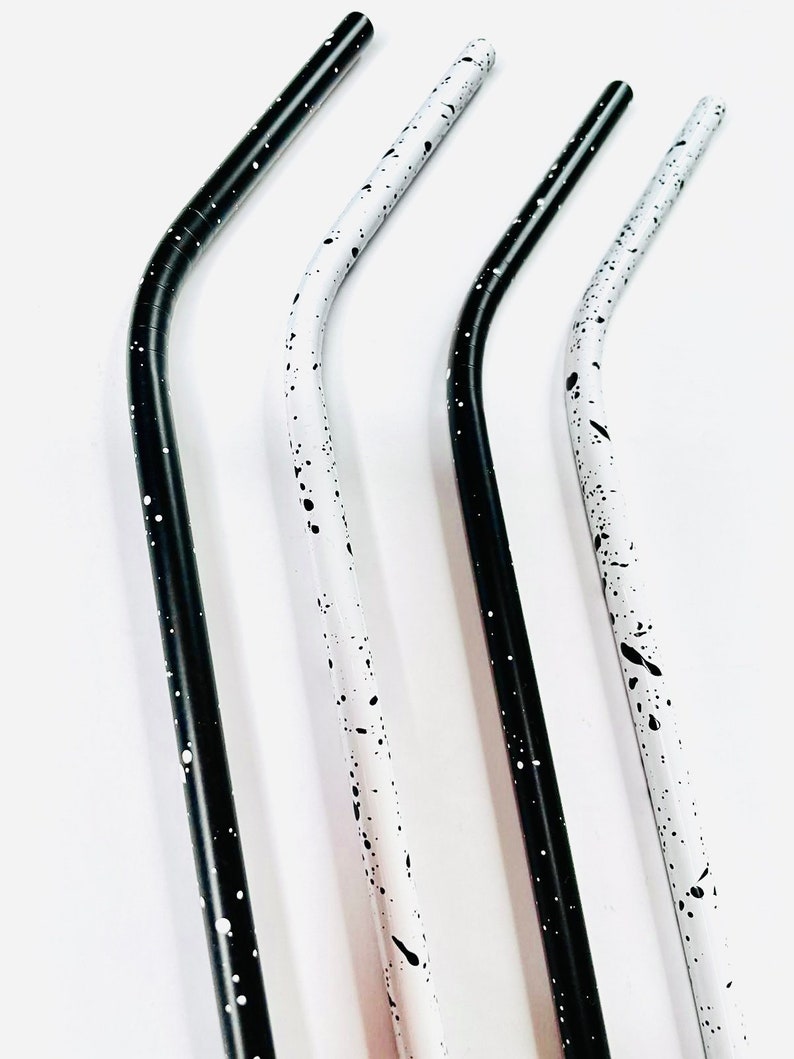 May include: Four stainless steel straws with a curved design. Two straws are black with white speckles, and two are white with black speckles. The straws are angled and appear to be reusable.