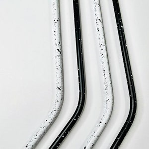 May include: Four reusable metal straws. Two are white with black speckles, and two are solid black. All straws have a curved design and are made of metal. The straws are designed for drinking beverages.