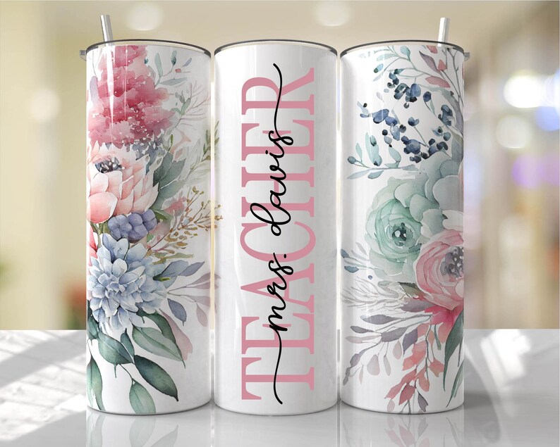 May include: Three stainless steel tumblers with floral designs. The center tumbler has the text "TEACHER miss davis" in pink lettering.