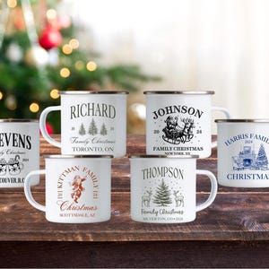 Peut inclure: Six tasses en émail blanc avec des motifs et du texte noirs et bleus. Les tasses présentent différents noms de famille et lieux, tels que "Stevens, Vancouver, C.-B." et "Famille Harris, Noël".