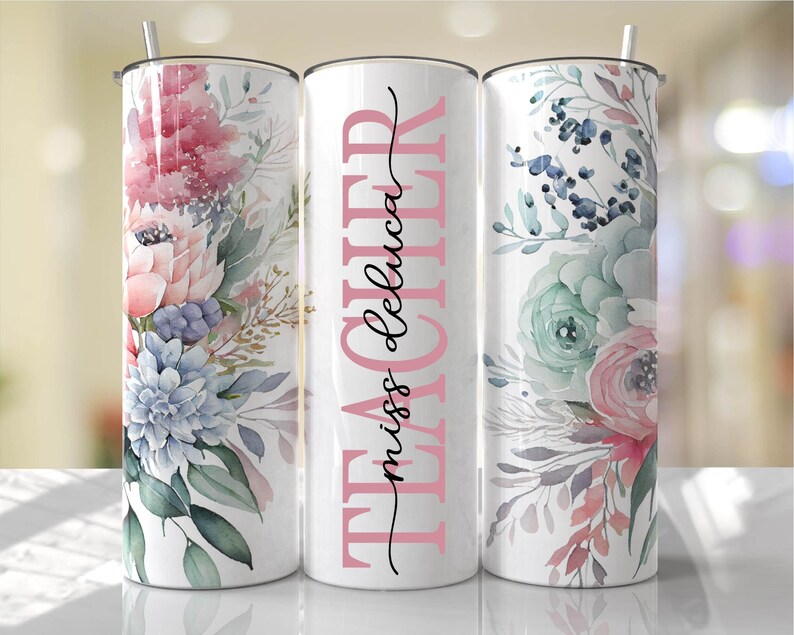 May include: Three stainless steel tumblers with floral designs. The middle tumbler has the text "TEACHER miss deluca" in pink and black lettering.