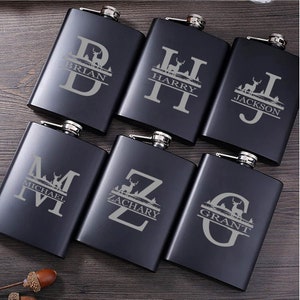 May include: Six black metal hip flasks with personalised engravings. Each flask features a different letter, a deer silhouette, and a name. The names are Brian, Harry, Jackson, Michael, Zachary, and Grant.