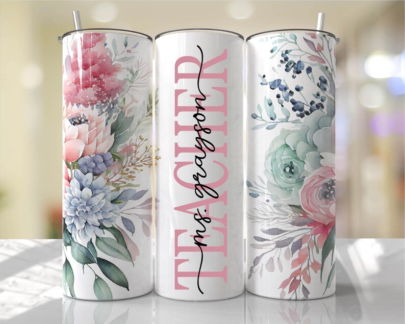 May include: Three stainless steel tumblers with floral designs. The middle tumbler has the text "TEACHER" in black with "mrs. grayson" in pink underneath.