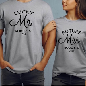 May include: A couple wearing matching grey t-shirts with the text "Lucky Mr. Roberts 2024" and "Future Mrs. Roberts 2024" in black.