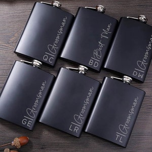 May include: Six black metal hip flasks with engraved initials and the word "Groomsman".