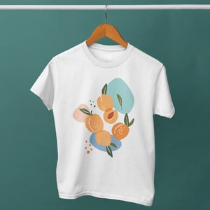 May include: White t-shirt with a graphic design of peaches and abstract shapes in shades of blue, orange, and pink.