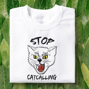 May include: White t-shirt with a black and white illustration of a cat with the text "STOP CATCALLING" printed on it.