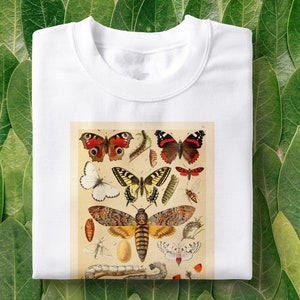 Op de afbeelding: Wit T-shirt met een vintage illustratie van verschillende vlinders en motten. De illustratie bevat een verscheidenheid aan kleuren, waaronder rood, geel, zwart en wit.