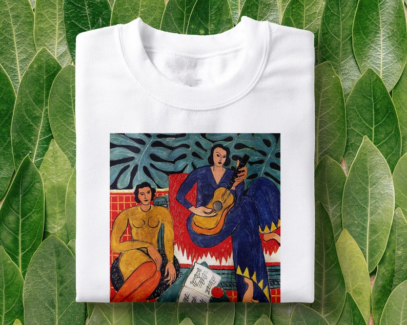 Puede incluir: Camiseta blanca con una pintura colorida de dos personas, una tocando la guitarra, sobre un fondo verde de hojas. La pintura es de estilo cubista con colores vivos y formas geom&eacute;tricas.